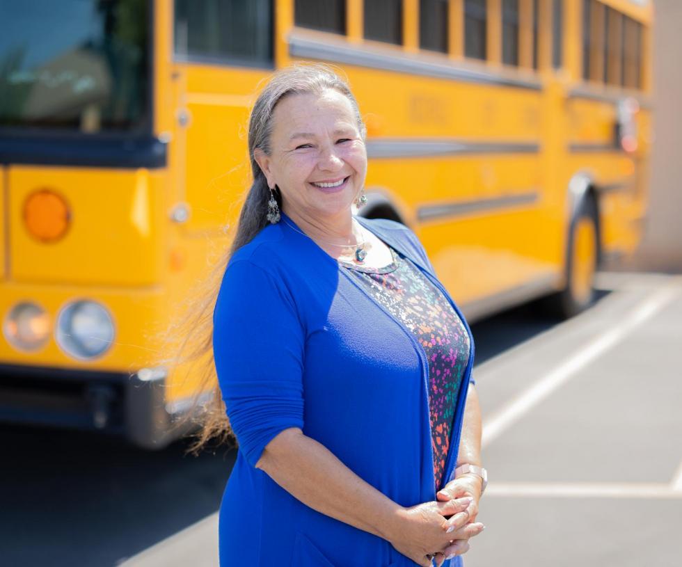 Smiling person standing in front of school bus in parking lot 