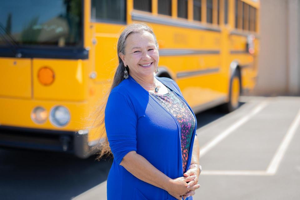 Smiling person standing in front of school bus in parking lot 